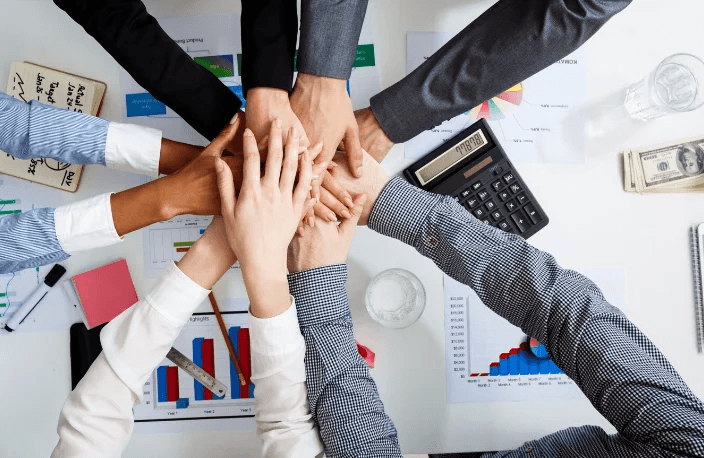 A team stacking hands together over desks with financial charts